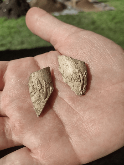 hand holding piece of clay pipe with ship carved